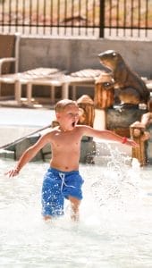 An excited kid enters the pool deck at a splash pad in North Carolina, water splashing beneath his feet.