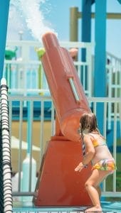 A little girl activates the spray of a water cannon pulling the rope at the water playground by Interactive Play.