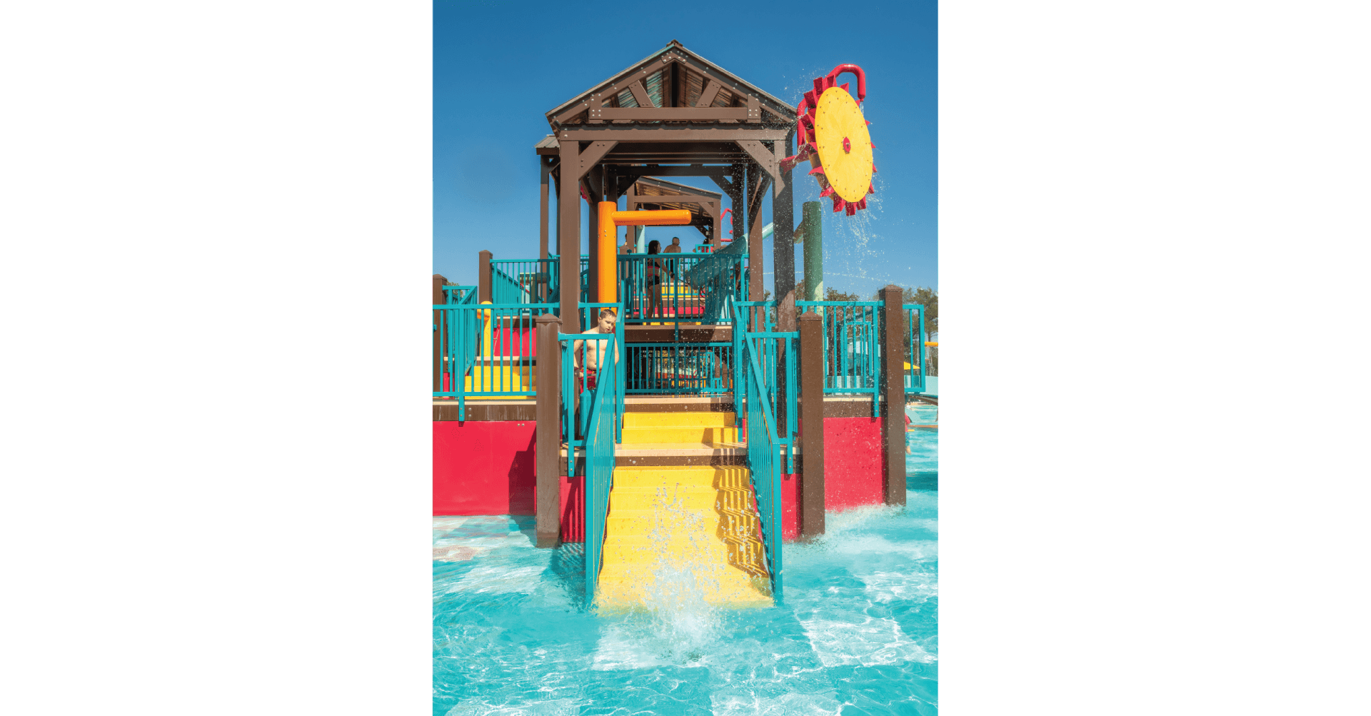 The Oh Chute water wheel spins, attached to one of the decks at the water play structure at the Jellystone in Tyler Texas, spraying water in a circular pattern onto the pool floor.