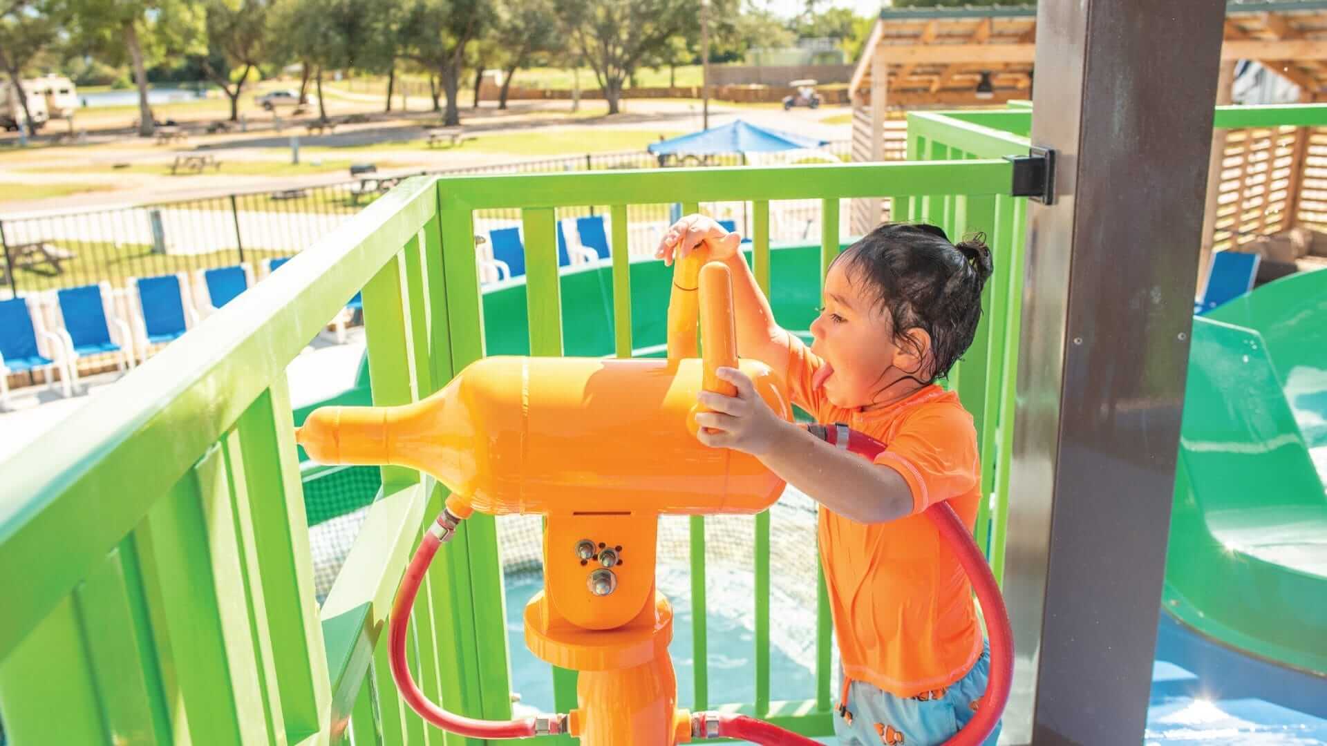 A toddler activating the rusher water gun from a deck on the water play structure built by Interactive Play in Waller, Texas.