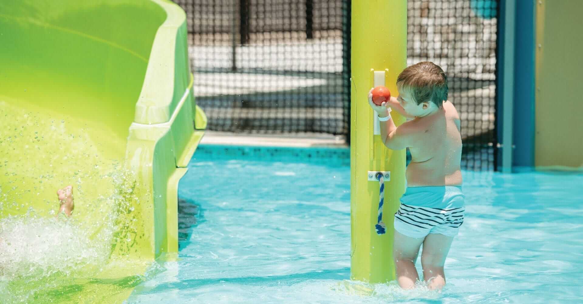 A little boy activates a water play feature pushing up on a lever.