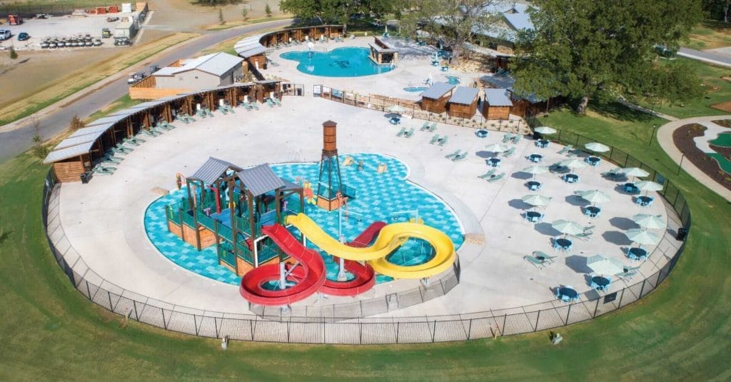 A wide angle shot of the entire aquatic play structure at the Camp Fimfo RV resort in waco, texas, showcasing the vast pool deck and cabana space surrounding the play unit.
