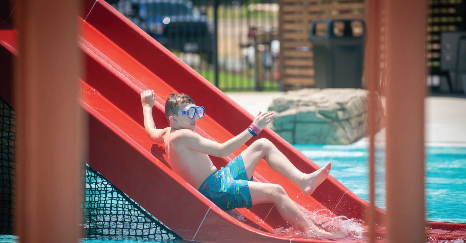 A kid slides down a water slide with swim goggles on at the Camp Fimfo RV Park in Waco Texas.