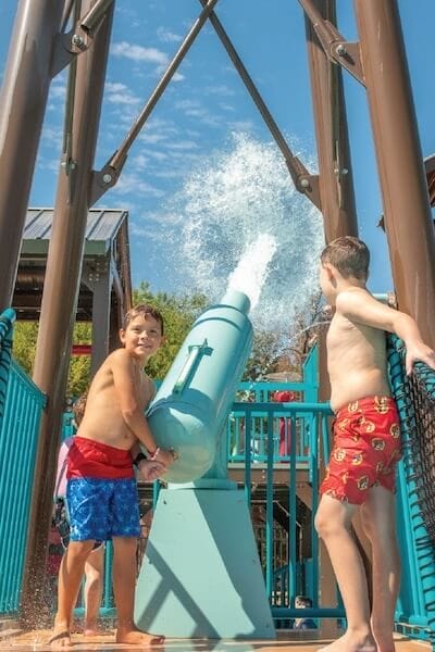 Two kids activate the cannon water feature creating a large burst of water propelled into the air after pulling the activation rope.